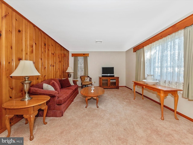 living area featuring light colored carpet, wood walls, visible vents, and baseboards