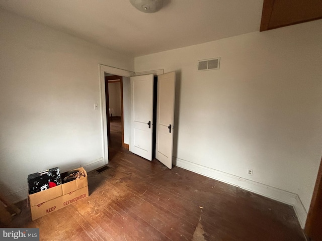 unfurnished bedroom with dark wood-style flooring, visible vents, and baseboards