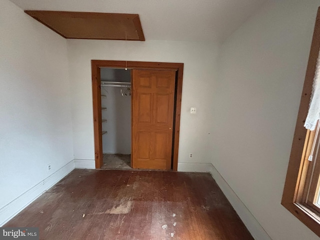 unfurnished bedroom with dark wood finished floors, attic access, and baseboards