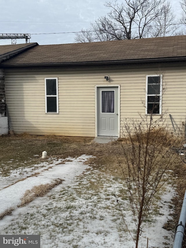 snow covered property entrance featuring roof with shingles