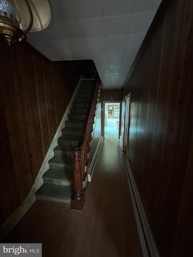 hallway featuring wooden walls, stairs, a baseboard heating unit, and dark wood-style floors