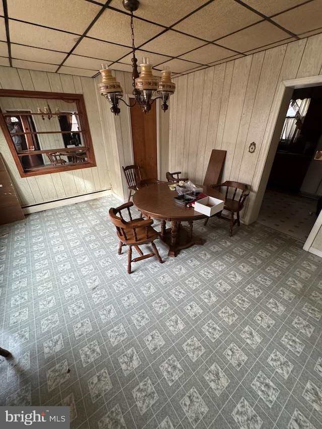 unfurnished dining area with a paneled ceiling, wood walls, and an inviting chandelier