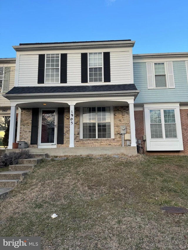 traditional home featuring a porch, a front yard, and brick siding