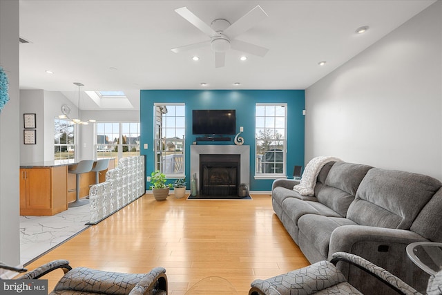 living room featuring a ceiling fan, lofted ceiling with skylight, a fireplace with flush hearth, light wood-style floors, and recessed lighting