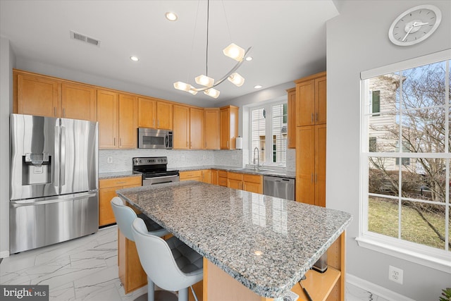 kitchen featuring marble finish floor, a kitchen island, appliances with stainless steel finishes, and a breakfast bar area