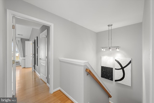 corridor with baseboards, an upstairs landing, and light wood-style floors