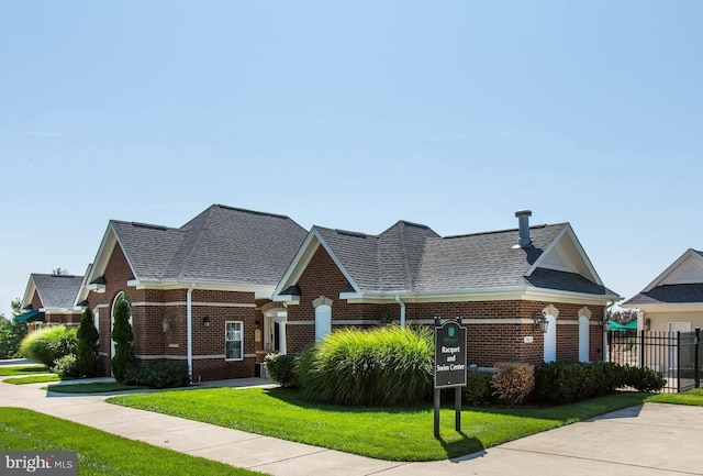 view of front facade featuring a shingled roof, a front yard, fence, and brick siding