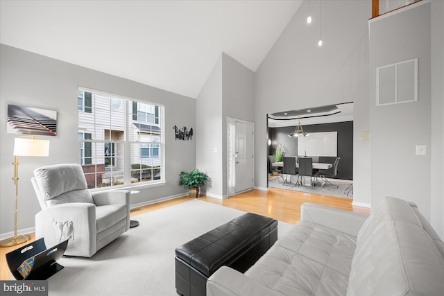 living area with high vaulted ceiling, visible vents, light wood-style flooring, and baseboards