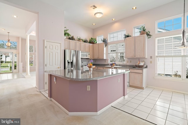 kitchen with light brown cabinetry, ornate columns, white appliances, a center island, and baseboards