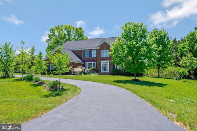 colonial house featuring brick siding, curved driveway, and a front lawn