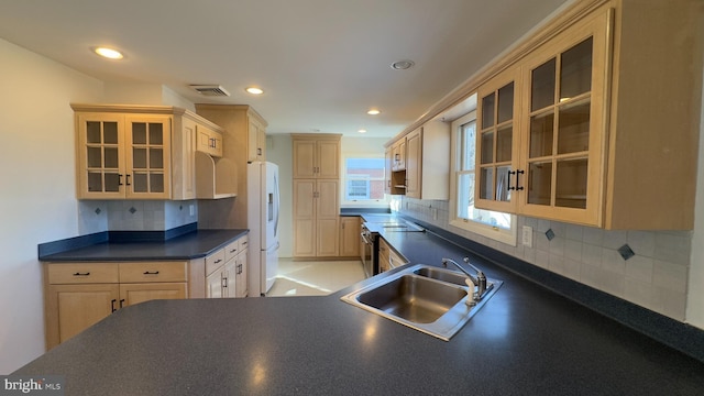 kitchen featuring dark countertops, white fridge with ice dispenser, glass insert cabinets, and a sink