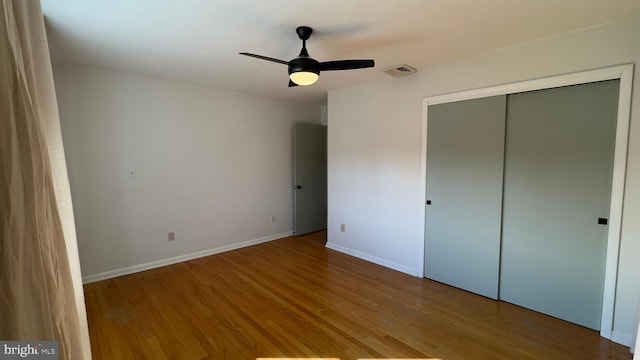 unfurnished bedroom with a closet, visible vents, a ceiling fan, wood finished floors, and baseboards