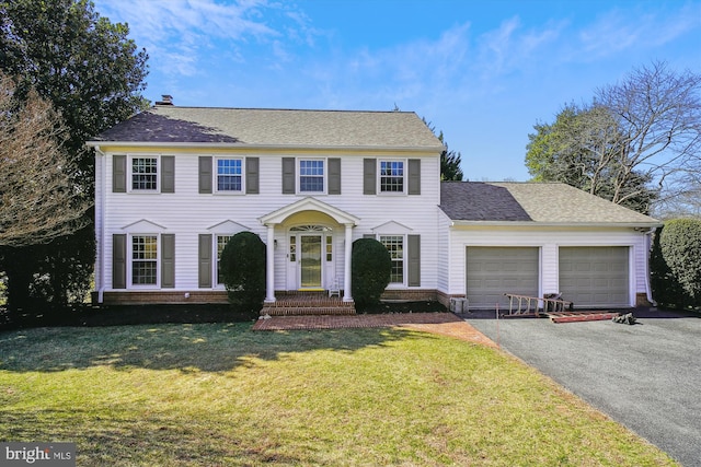 colonial home with aphalt driveway, roof with shingles, a front yard, a garage, and a chimney