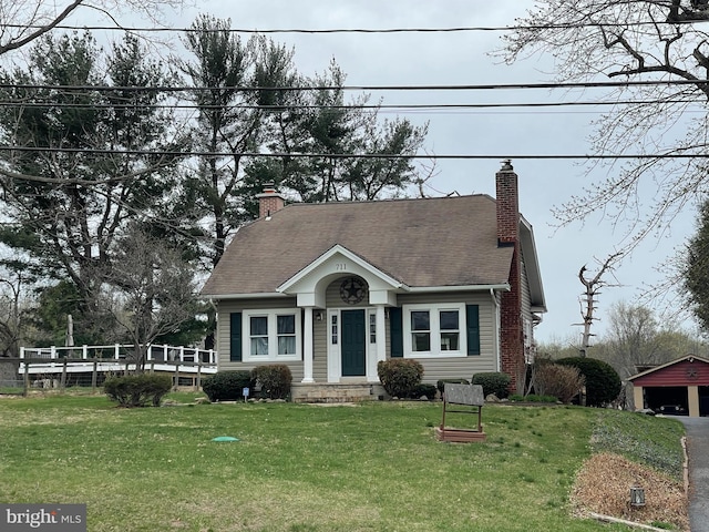 cape cod-style house featuring a chimney, an outbuilding, a detached garage, and a front yard