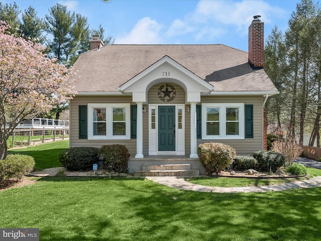 view of front of house with a chimney, a front lawn, and roof with shingles