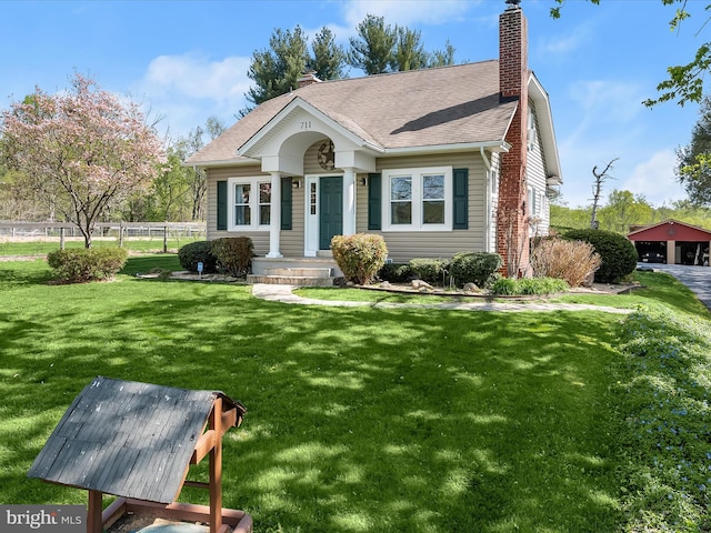 view of front of property with a chimney, a front lawn, a shingled roof, an outdoor structure, and fence