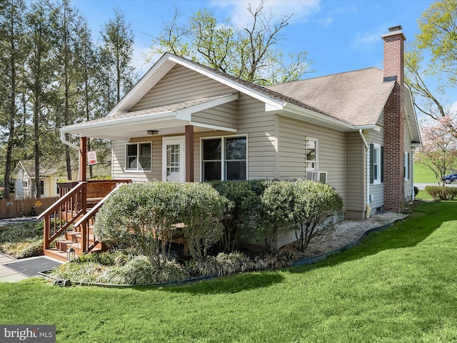 view of front facade featuring a chimney, a front lawn, covered porch, and a shingled roof