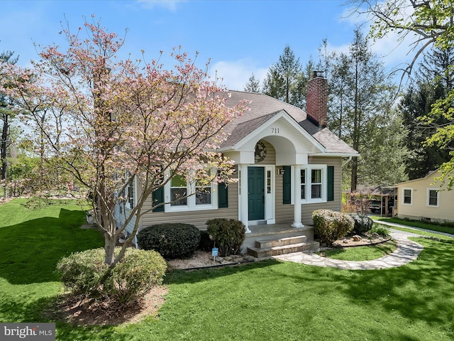 bungalow-style home featuring a shingled roof, a front lawn, and a chimney