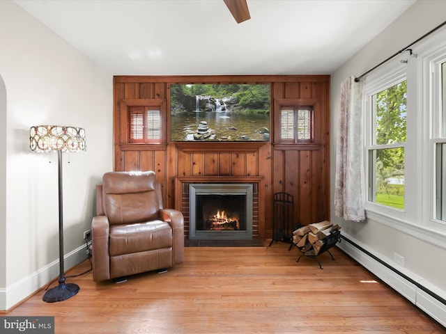 sitting room featuring baseboard heating, baseboards, a brick fireplace, and light wood-style floors