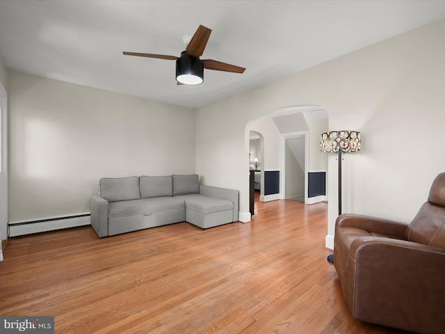 living room with a baseboard radiator, light wood-style floors, ceiling fan, arched walkways, and baseboards