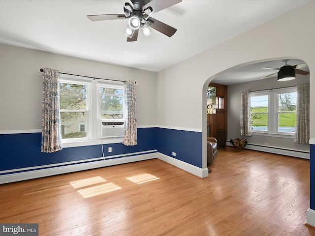 unfurnished room with arched walkways, wood finished floors, a ceiling fan, and baseboard heating