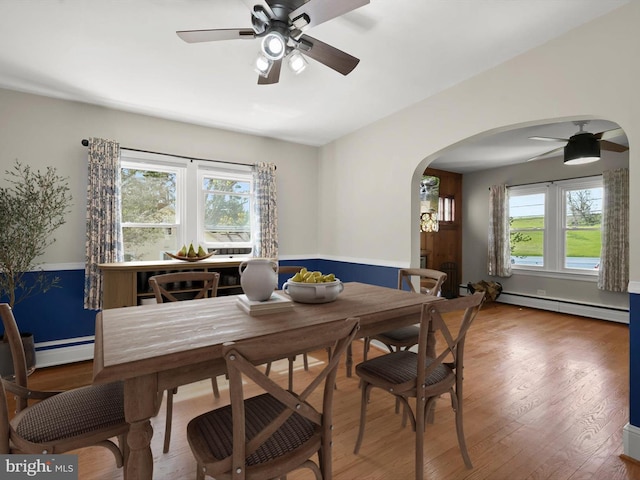 dining area featuring a baseboard heating unit, arched walkways, a ceiling fan, and wood finished floors