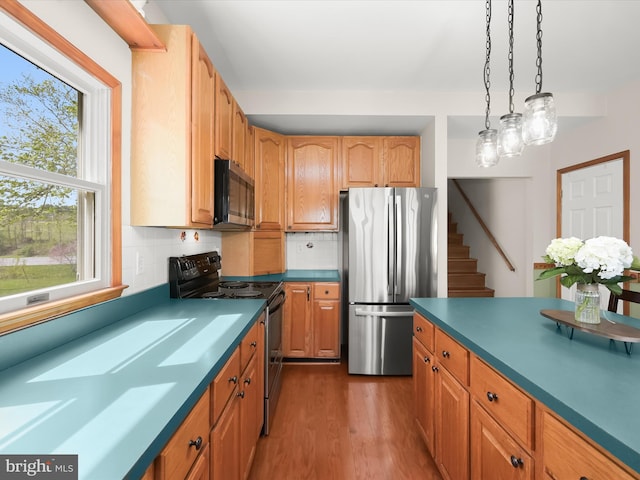 kitchen featuring dark wood-style flooring, decorative backsplash, hanging light fixtures, and stainless steel appliances