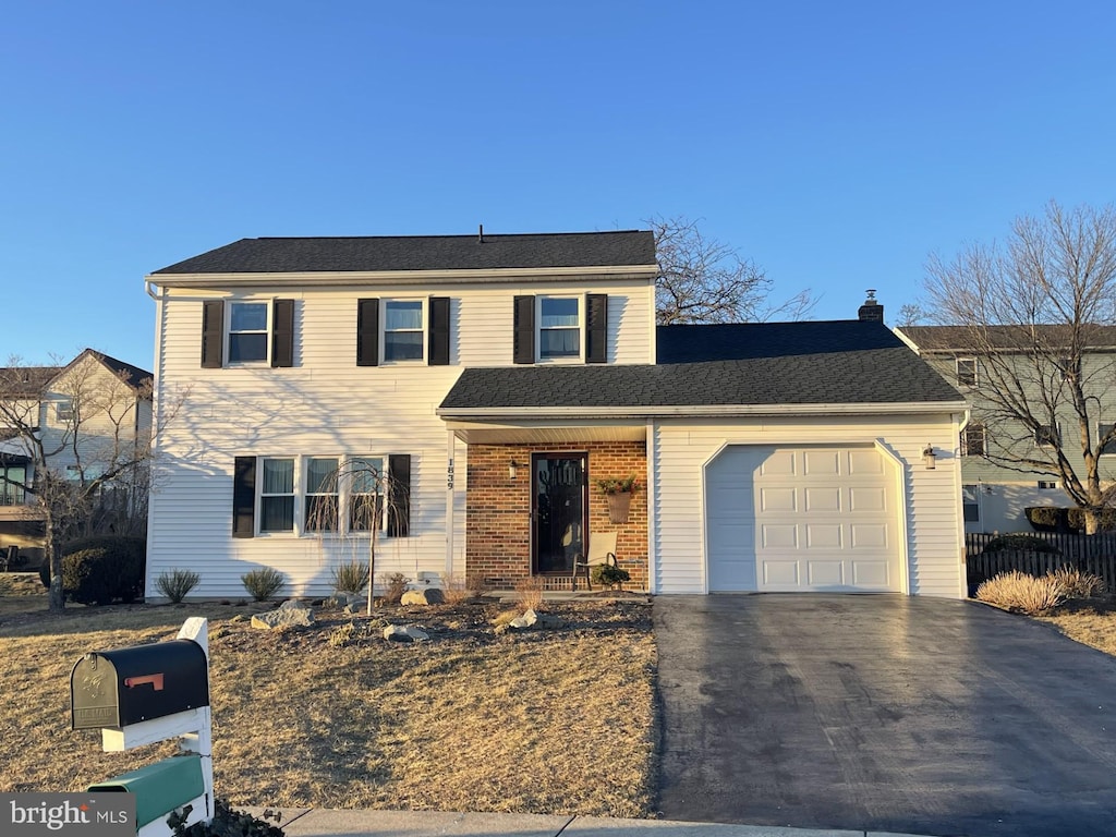 traditional-style home with a garage, aphalt driveway, a chimney, and brick siding