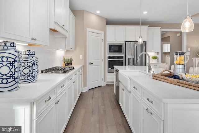 kitchen featuring a center island with sink, white cabinets, wood finished floors, hanging light fixtures, and stainless steel appliances