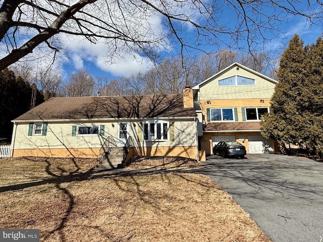 view of front facade featuring aphalt driveway, a chimney, and an attached garage