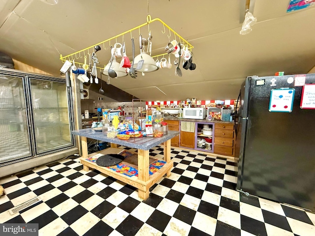 kitchen featuring lofted ceiling, white microwave, freestanding refrigerator, tile patterned floors, and brown cabinetry