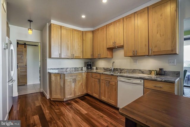 kitchen featuring a barn door, dark wood-style flooring, freestanding refrigerator, white dishwasher, and a sink