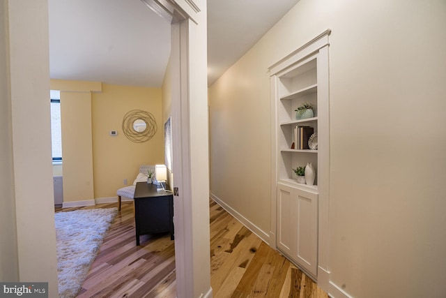 hallway featuring baseboards, wood finished floors, and built in features