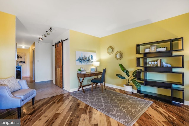 sitting room with track lighting, wood finished floors, baseboards, and a barn door