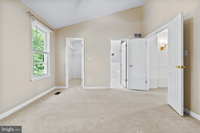 unfurnished bedroom featuring a walk in closet, visible vents, baseboards, lofted ceiling, and carpet