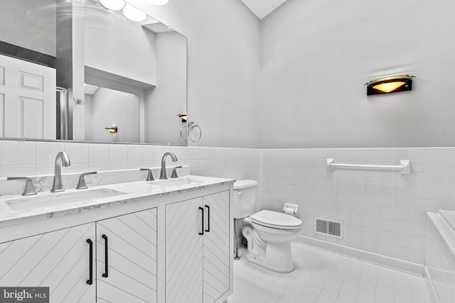 full bath with visible vents, a sink, wainscoting, and tile walls