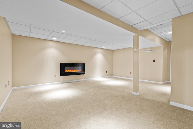 finished basement featuring visible vents, a paneled ceiling, baseboards, a glass covered fireplace, and carpet