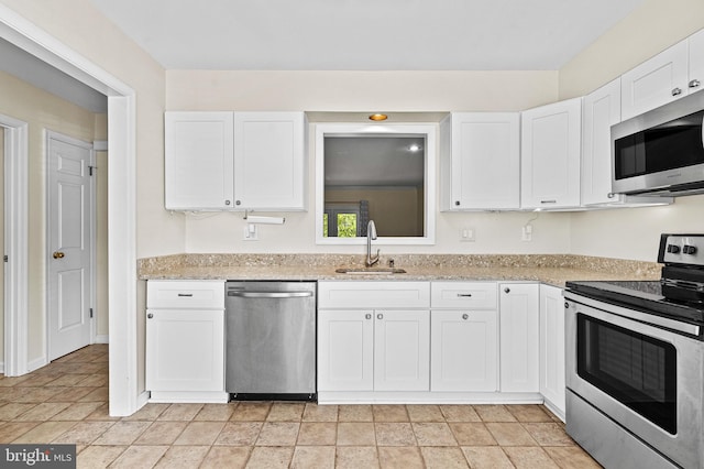 kitchen featuring stone finish flooring, appliances with stainless steel finishes, a sink, light stone counters, and white cabinets