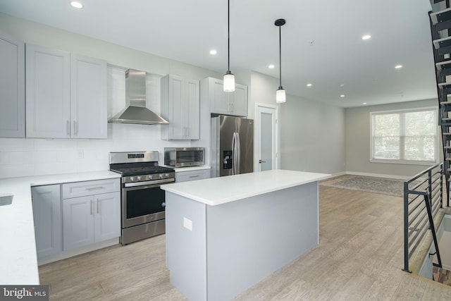 kitchen with appliances with stainless steel finishes, light countertops, wall chimney range hood, and light wood finished floors