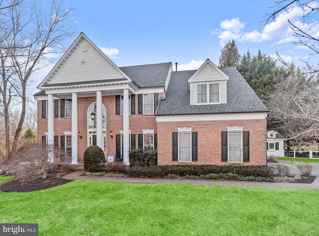 neoclassical / greek revival house with roof with shingles, a front yard, and brick siding