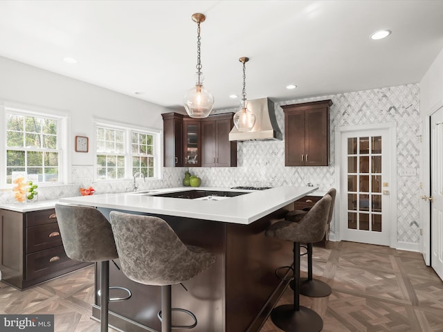 kitchen with light countertops, a kitchen breakfast bar, dark brown cabinetry, and premium range hood