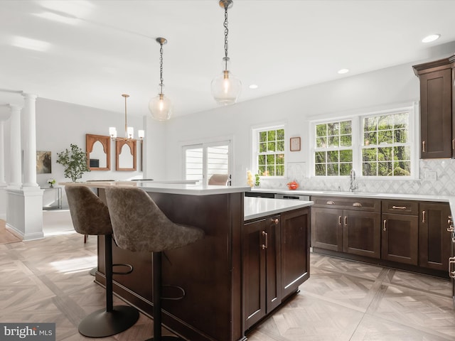 kitchen with a sink, light countertops, a kitchen breakfast bar, a center island, and ornate columns