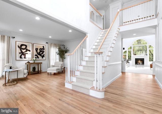 stairway with a high ceiling, a lit fireplace, ornamental molding, and wood finished floors