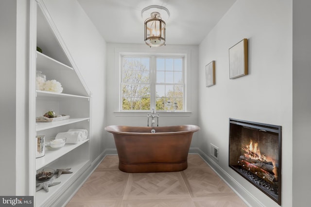 full bath with a freestanding bath, baseboards, a lit fireplace, and visible vents