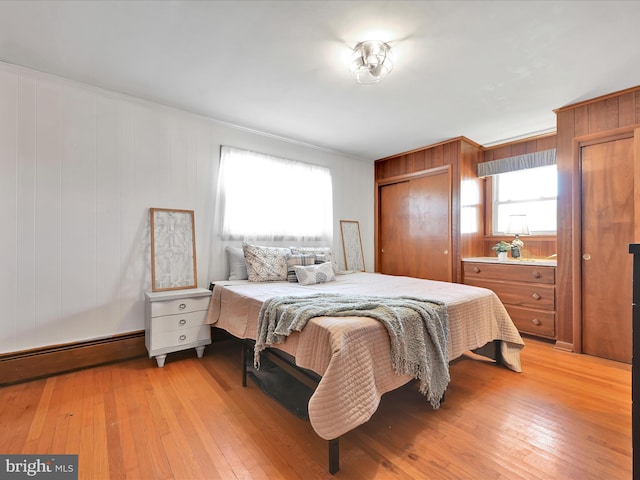 bedroom with light wood finished floors, baseboard heating, and multiple closets