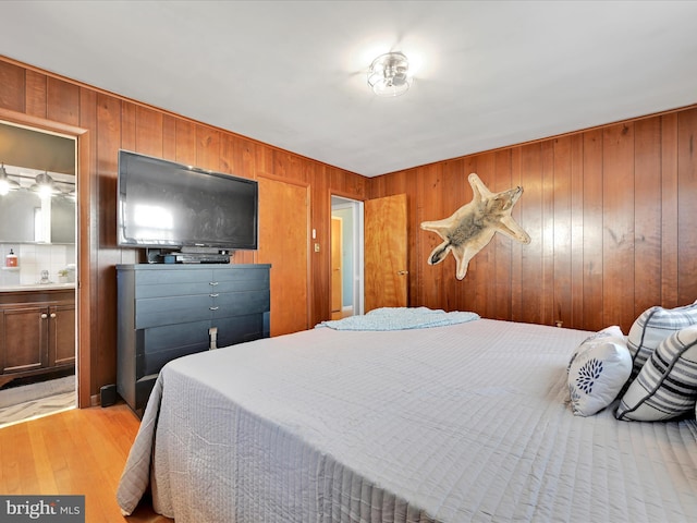 bedroom featuring wood walls, light wood-style flooring, and ensuite bathroom