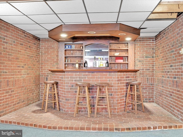 bar with a dry bar, brick wall, and a drop ceiling