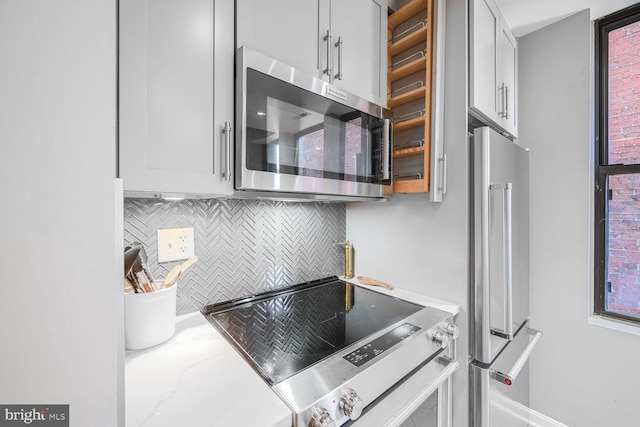 kitchen with decorative backsplash, white cabinets, light stone countertops, and appliances with stainless steel finishes