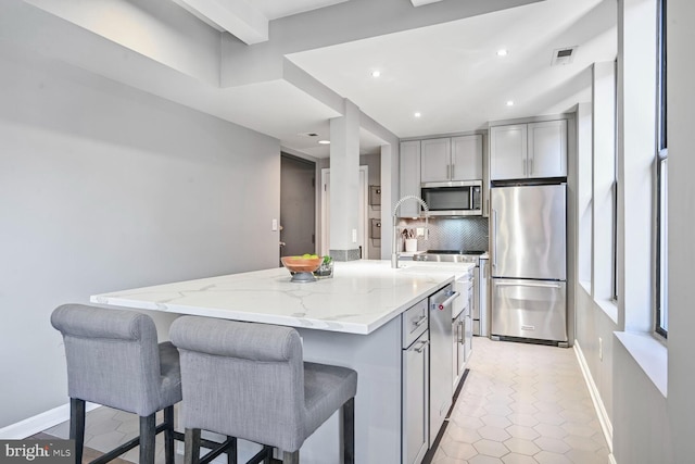 kitchen featuring visible vents, gray cabinets, light stone counters, tasteful backsplash, and stainless steel appliances