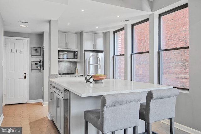 kitchen featuring beverage cooler, visible vents, gray cabinets, decorative backsplash, and stainless steel microwave